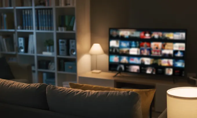 Living room with soft warm lamp by a TV screen displaying various shows to watch on a streaming service