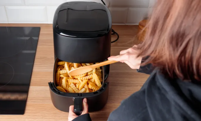 Woman at home using air fryer machine.