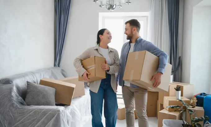 A young couple holds cardboard boxes as they prepare to move to their new home.