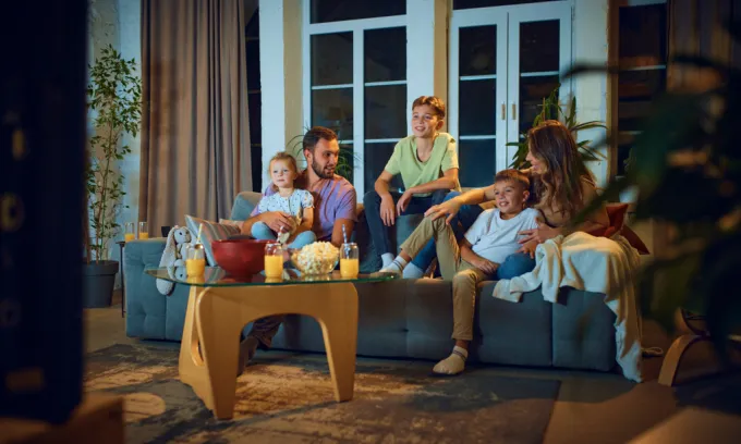 A young family gathered on the couch, with popcorn and orange juice, ready to stream a movie