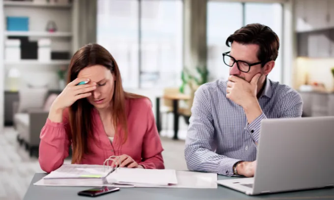 Young couple sitting in kitchen stressed about financial troubles and bills.