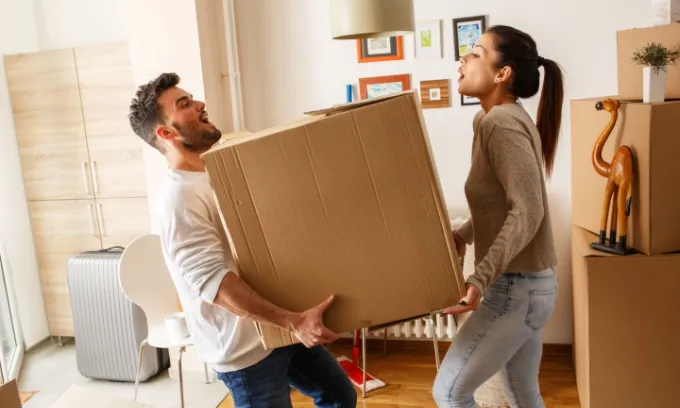 A young couple carries a moving box into their new home.
