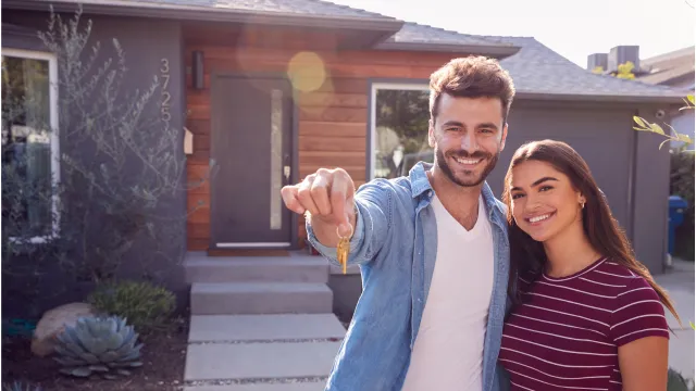 A happy young couple stand in front of their new home.