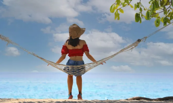 A woman sits on a hammock on a beach.