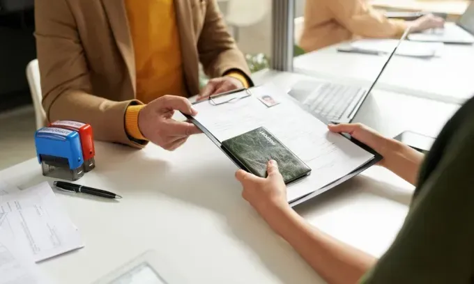A person hands a clipboard of passport documents to a professional