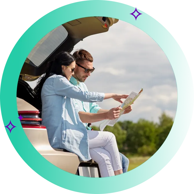 Two travellers navigating a printed map, seated on the boot of their car