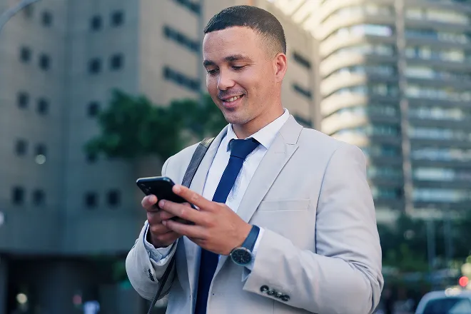 Man in a suite holding his phone and smiling while comparing mobile plans