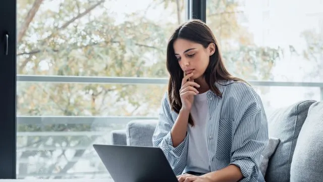 Concentrated millennial girl sit on couch working on laptop researching no credit check personal loans