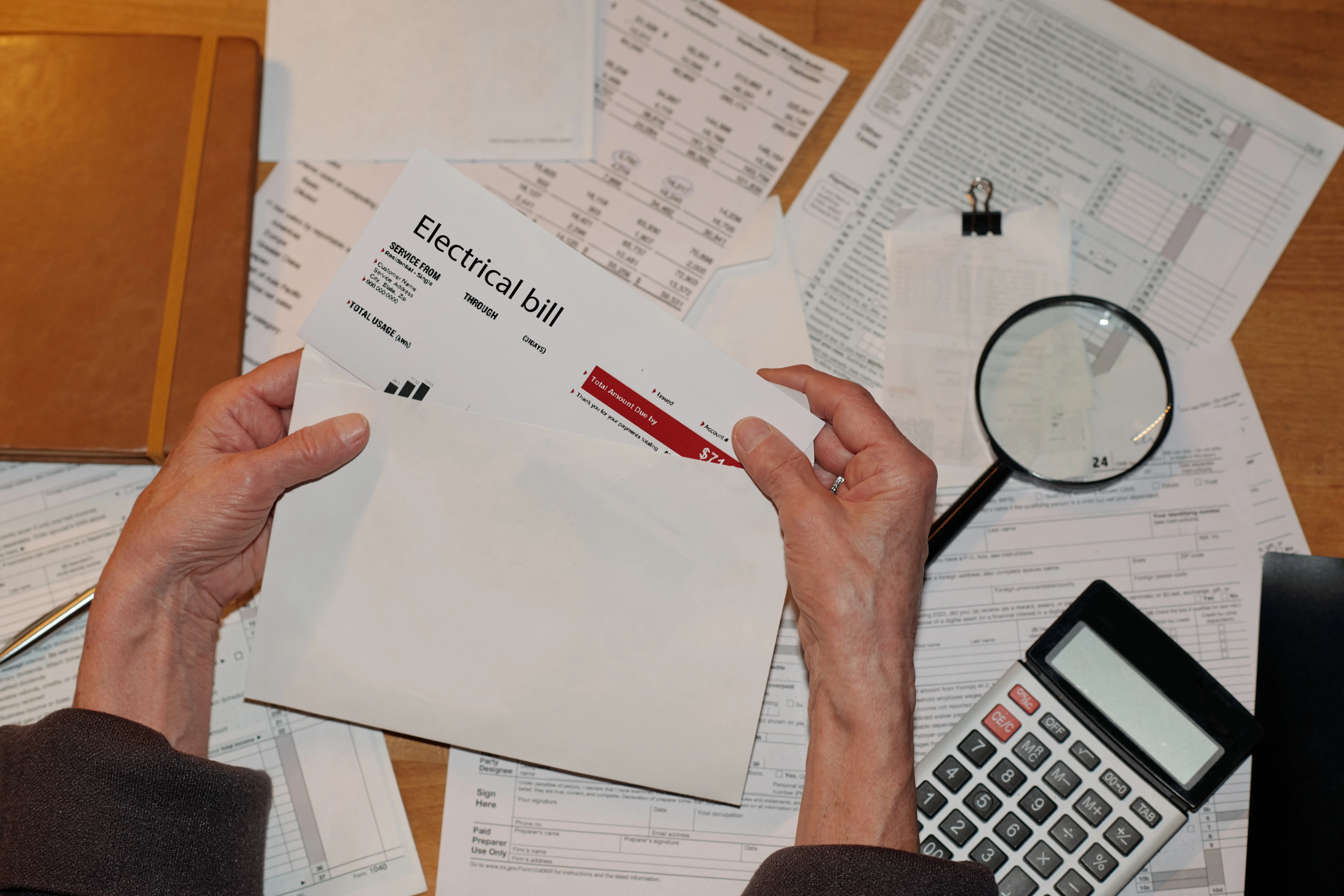 Top view of hands of senior unrecognizable woman taking electrical bill out of unpacked envelope over table with other financial bills