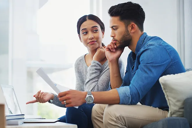 Young couple contemplating finances on sofa with laptop