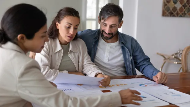 Financial advisor giving consultation to customers, showing analytics on paper diagrams, discussing saving strategy, insurance program. Broker presenting investment plan to couple