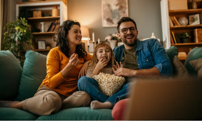 Young family eating popcorn and enjoying free streaming services on their laptop