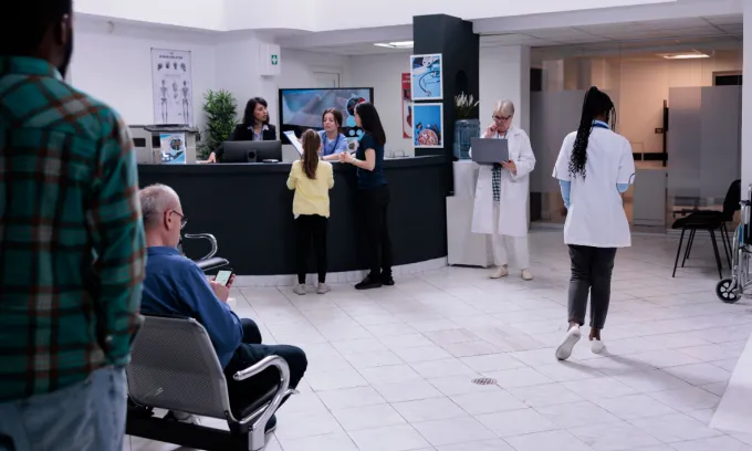 Hospital front desk reception with mother and child filling in form for doctor appointment .
