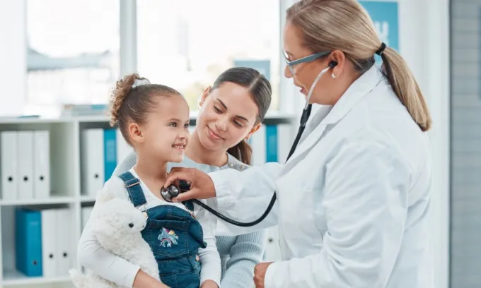 A doctor uses a stethoscope on a young girl who's being held by her mother