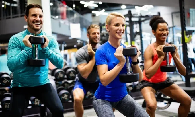 A group of people doing squates with a dumbell in a fitness class