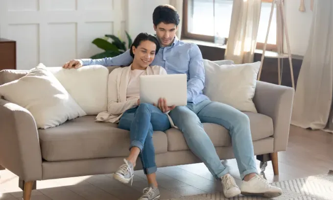 A young couple sits on the couch and looks at the cost of home insurance.