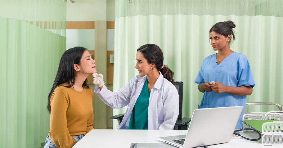 Female doctor examines face of cosmetic surgery patient while female assistant watches.