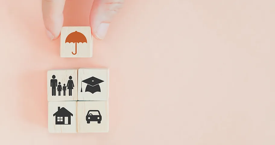 Fingers holding wooden blocks featuring an umbrella icon above family, house, graduation hat and car symbol for insurance concept