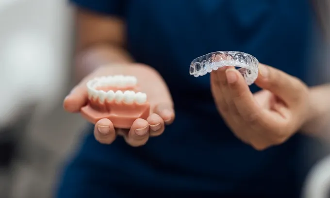 A dentist holds a set of fake teeth and an Invisalign retainer.