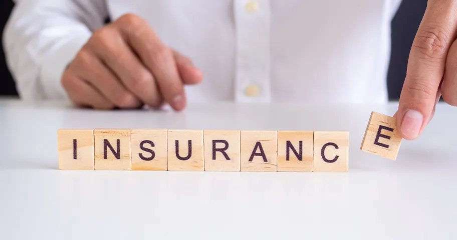 Close up of man's hand spelling out insurance out of wooden tiles
