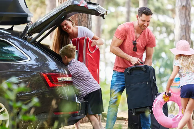 A family of four packing luggage into the trunk of their car, about to embark on a road trip.