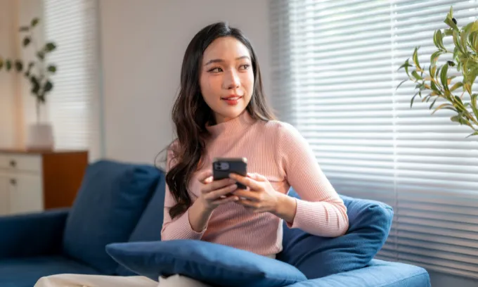 Young woman sitting on her couch reviewing data only SIM plans on her phone