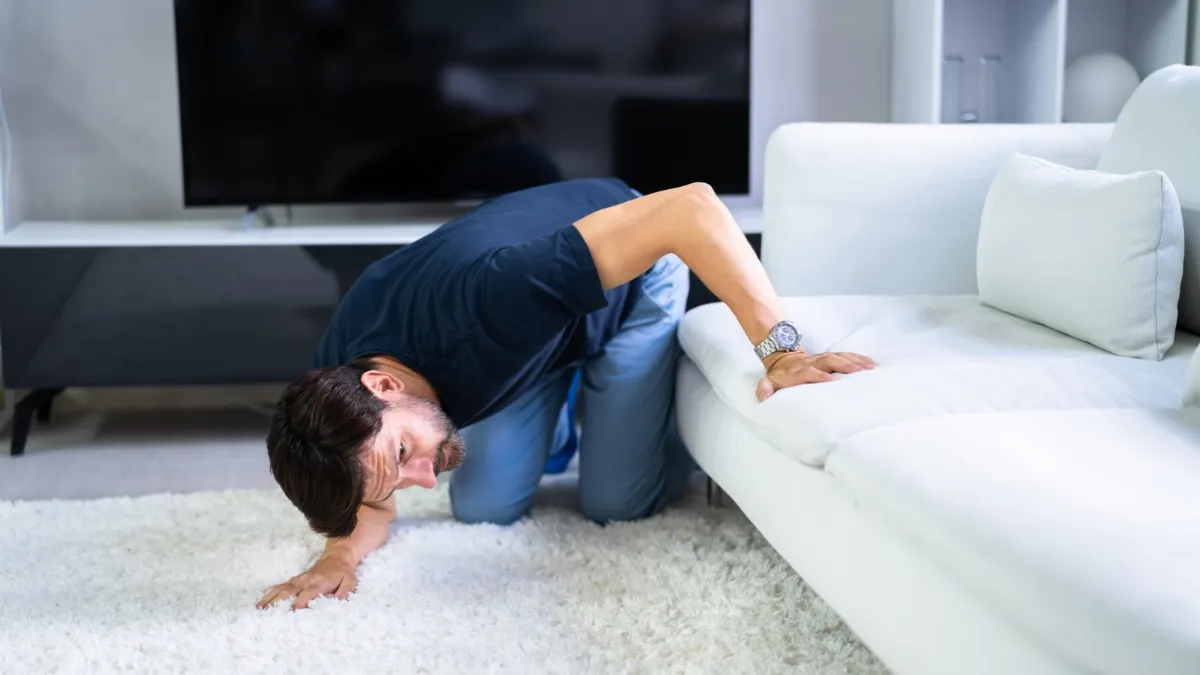 A man looks under his couch for lost money.