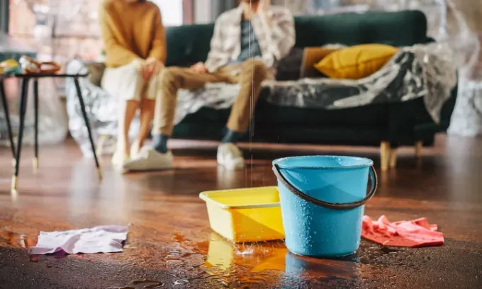 Water Drips into Buckets in Living Room. Couple in Background Calling Insurance Company.