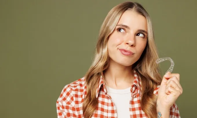A woman holds an Invisalign aligner in her hand contemplating her orthodontic decisions.