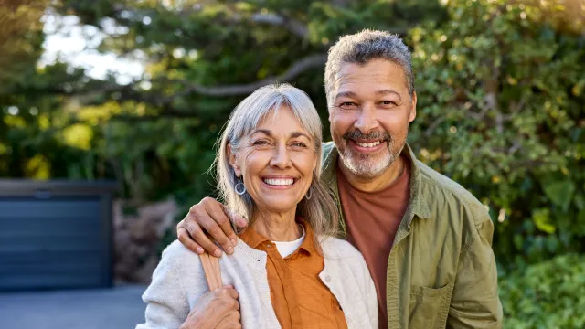 A happy older couple standing together smiling on the driveway of their house.