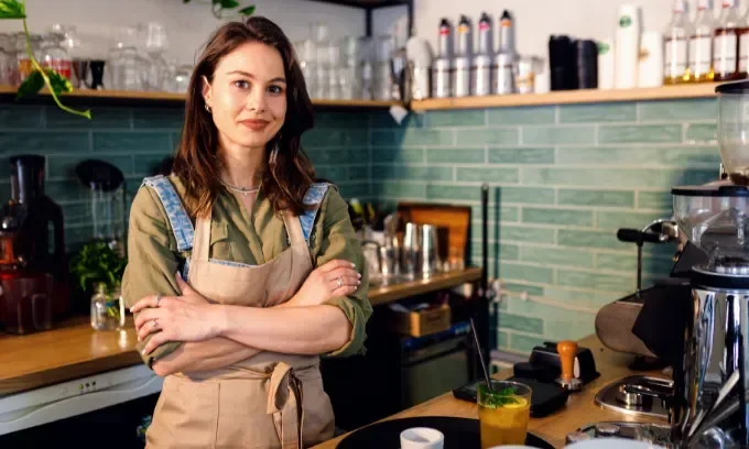 Female barista standing in her coffee shop behind the counter.