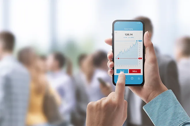 Close-up of mobile phone share trading app against background crowd