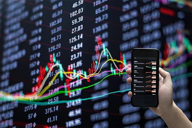 Mobile phone share trading app against background of stock prices and graph