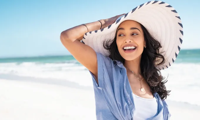 Carefree woman with white and blue straw hat walking at beach.