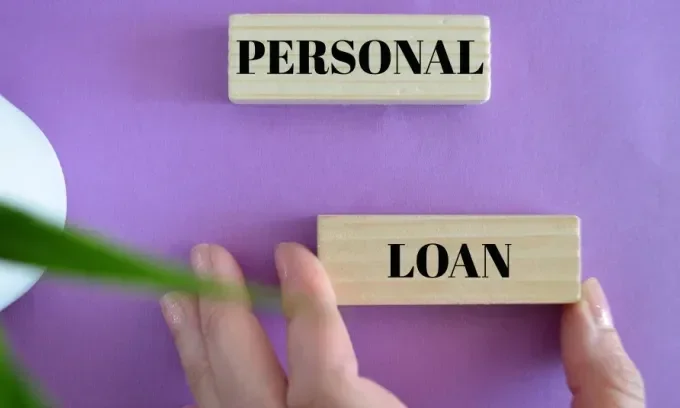 A hand holds a wooden block with the word 'loan' written on it in black letters. A similar block with the word 'personal' sits above it.