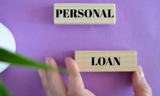 A hand holds a wooden block with the word 'loan' written on it in black letters. A similar block with the word 'personal' sits above it.