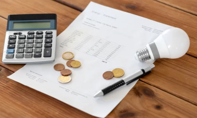 Energy bill with calculator, coins, a pen and a light bulb surrounding it.