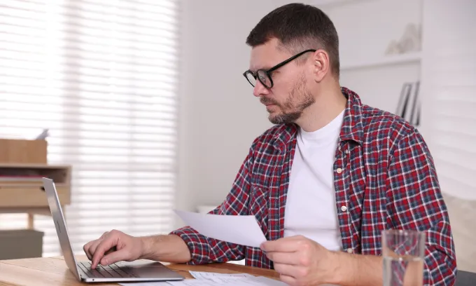 Man with laptop and calculator paying bills.
