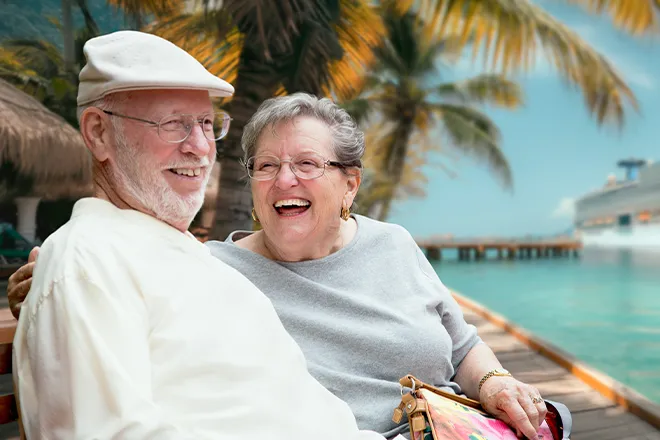 Happy elderly couple sitting on dock in tropical port with cruise liner in background