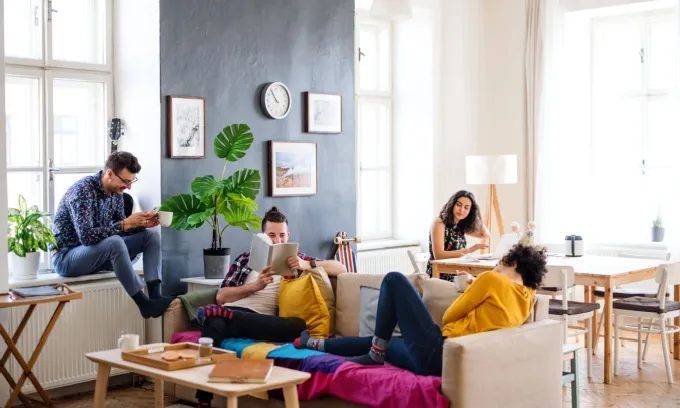 Four young adults relaxing, working, and reading together in a furnished living room.