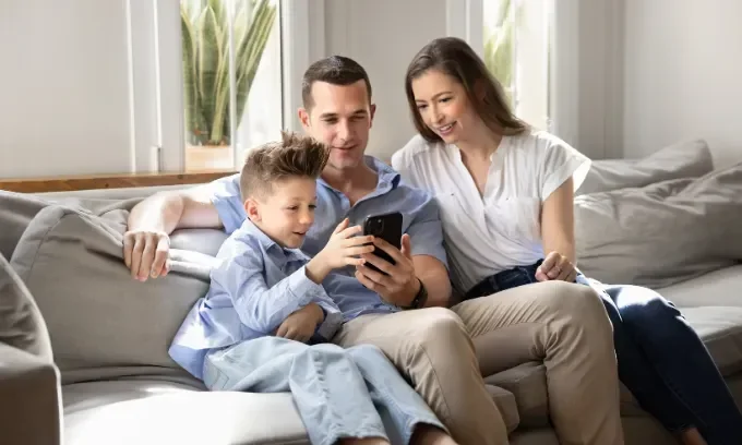 Family sitting on couch together looking at phone.