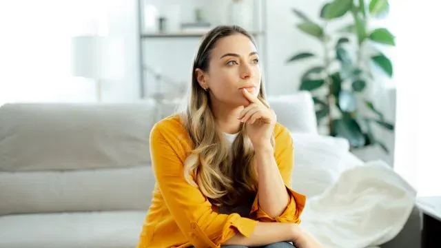 A woman sits on a couch and thinks about the pros and cons of personal loans.