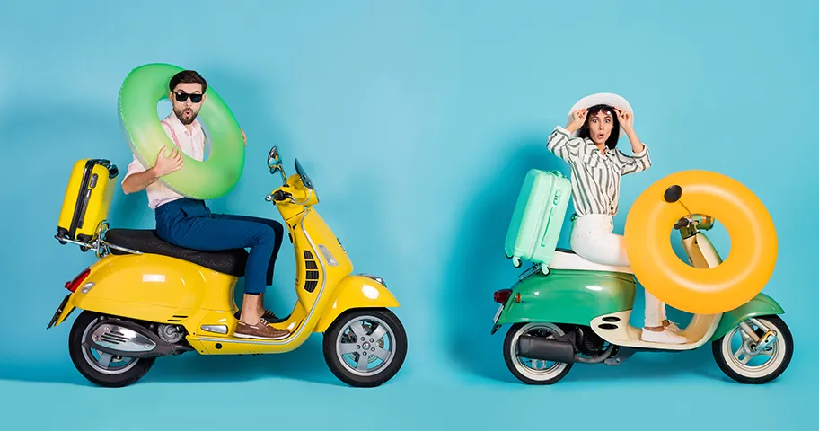 Couple in studio sitting on mopeds with holiday luggage