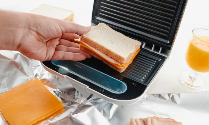 Person placing a ham and cheese sandwich into a toastie maker