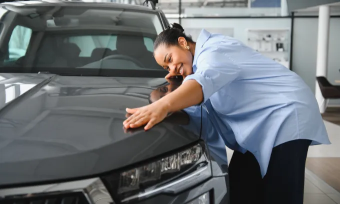 Cheerful lady embracing her new car in a dealership