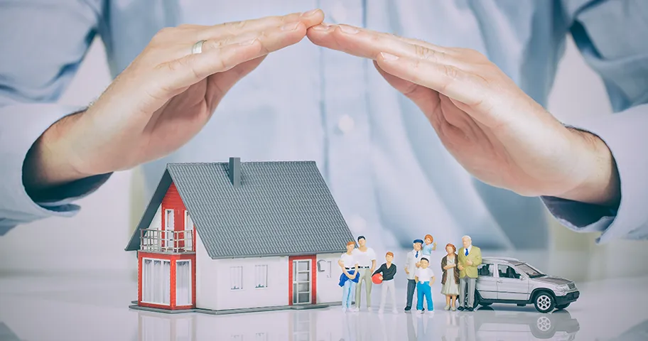 Hands forming protective roof over model of house, car and family members