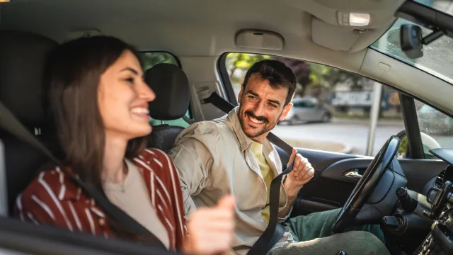 Happy adult man putting a seatbelt on in his car accompanied by his girlfriend.