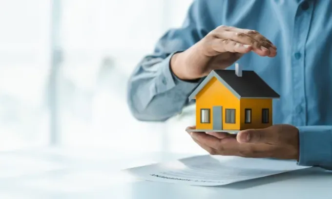 A landlord holds a model house and protects it with their other hand.