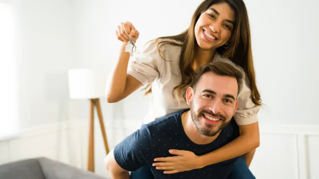 Man piggybacking his girlfriend showing their new home keys after buying a house