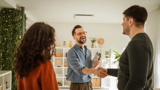 A couple shake hands with their real estate agent after agreeing to pay their deposit.